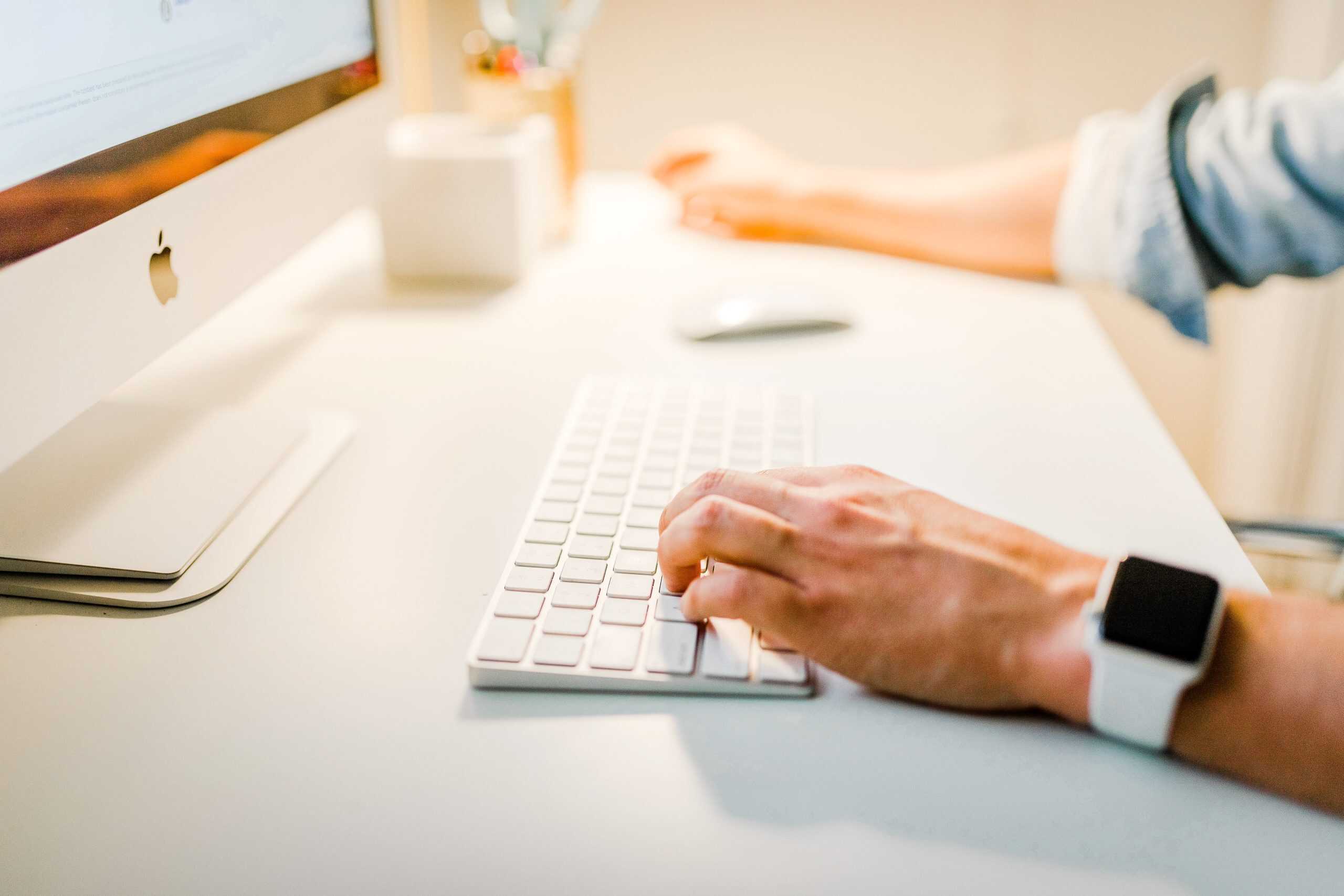 Handing typing on a keyboard with iMac showing on white desk